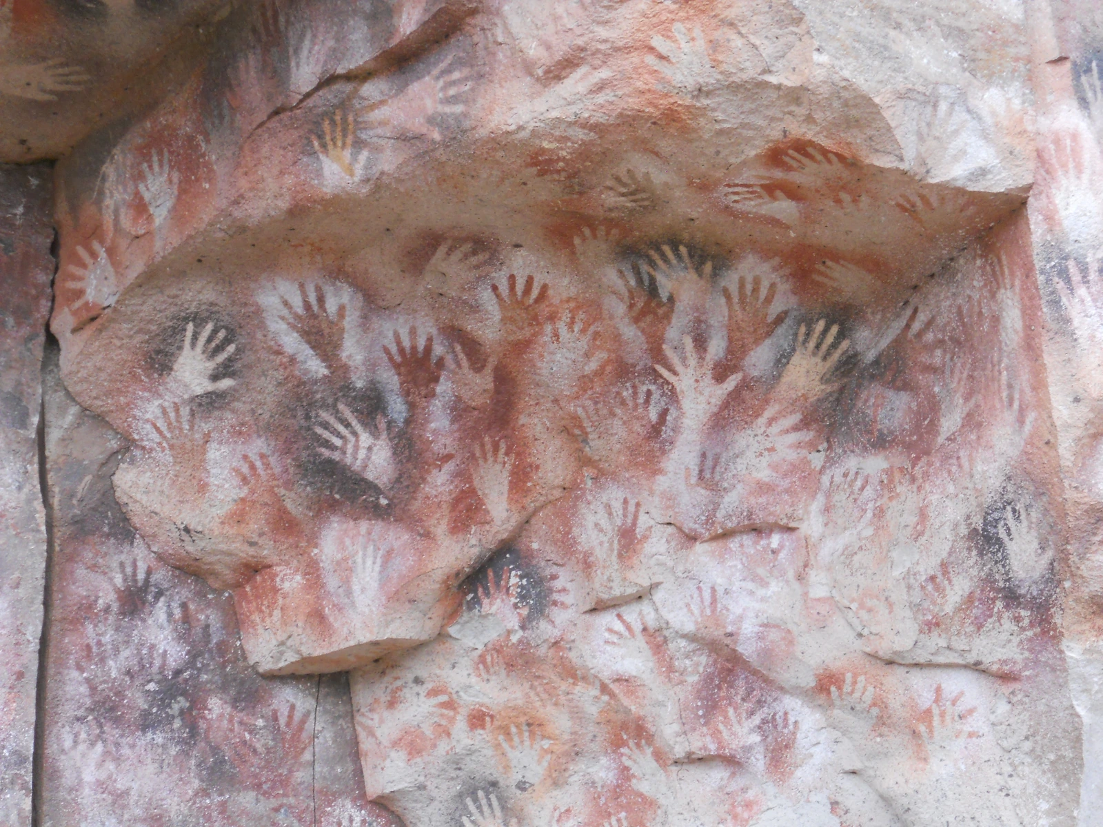 Negativos de manos blancas, rojas y oscuras sobre roca en Cueva de las Manos