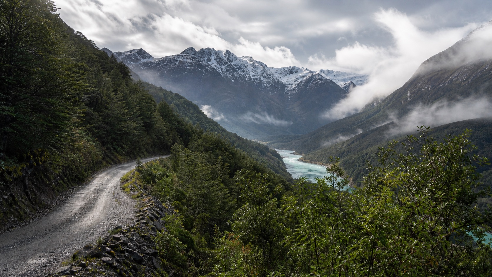 Camino de ripio de la Carretera Austral junto a bosque nativo, río glacial y montañas de Aysén
